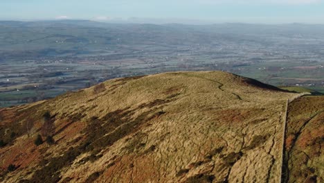 Early-sunlight-on-highland-mountain-peak-aerial-view-across-vast-frosty-idyllic-farmland-countryside-left-orbit