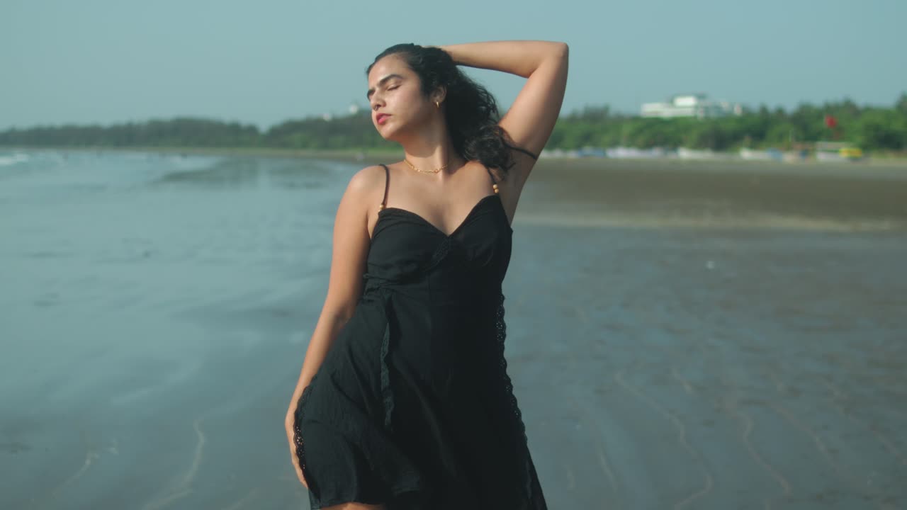 Front view of woman adjusting hair on quiet beach with soft daylight