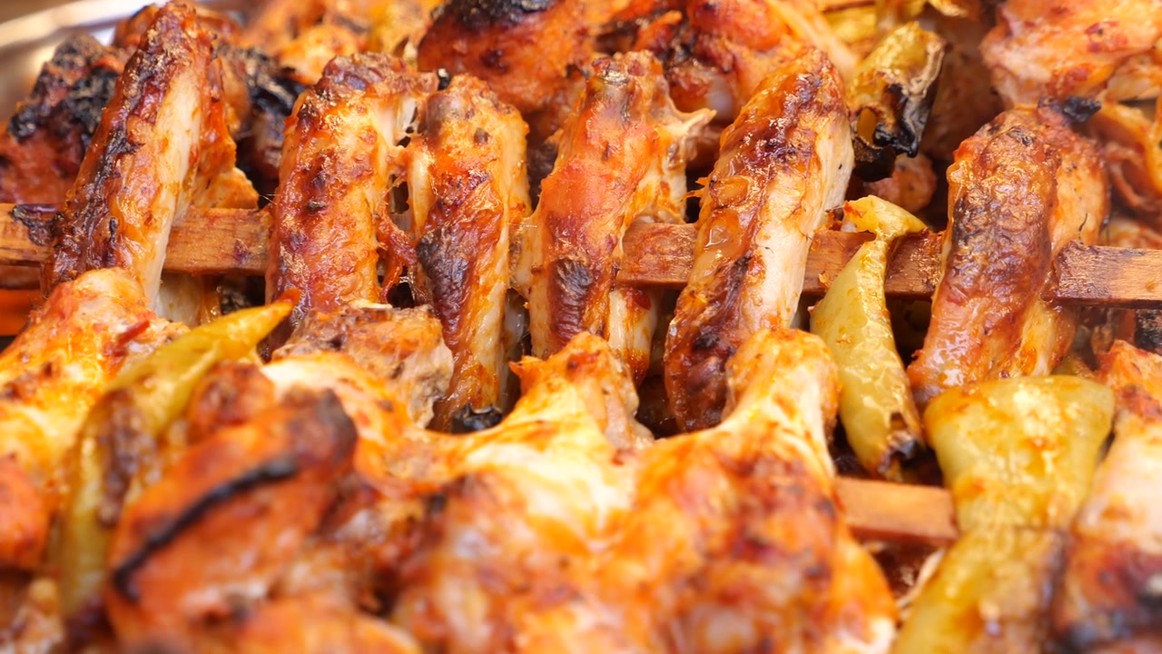 Primo piano di appetitose ali e cosce di pollo grigliate su spiedini