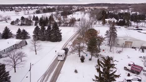 hauling white horse trailer through small winter town in michigan, aerial drone shot