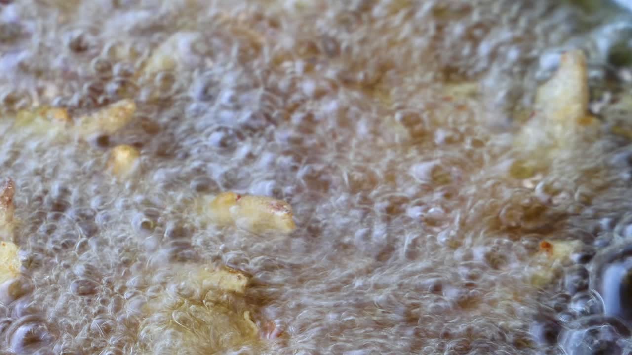Golden potato fries rapidly fry in bubbling oil, close-up, with bright natural lighting, minimal movement