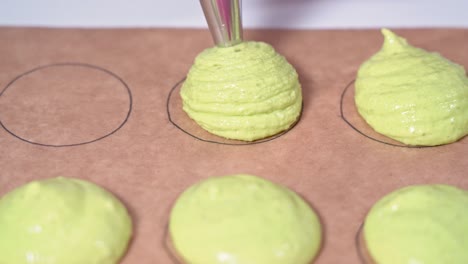 baker using a pastry bag to fill out circular shapes on parchment paper with a different colored shade of pink batter. making of macarons.