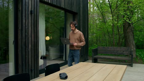 man working outdoors on a laptop in a modern wooden house