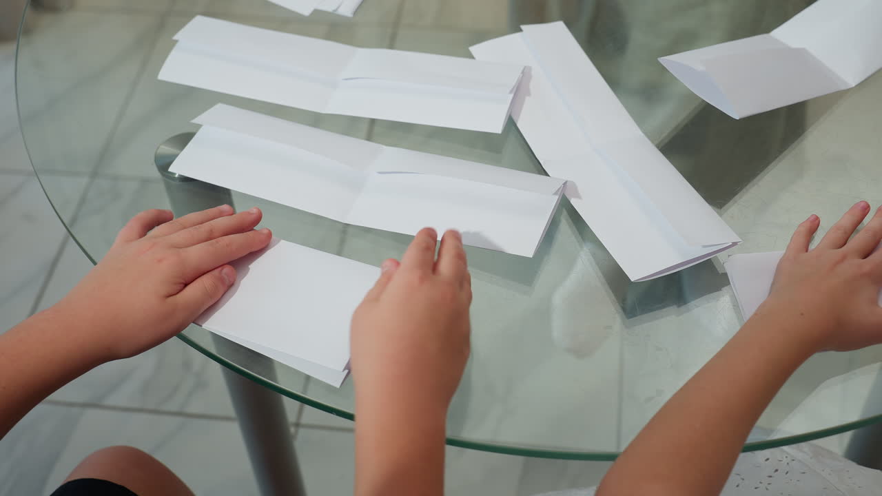 Hands of kids folding paper carefully on table, surrounded by folded paper and crafting tools, focus on hands engaged in paper folding in a cozy home environment