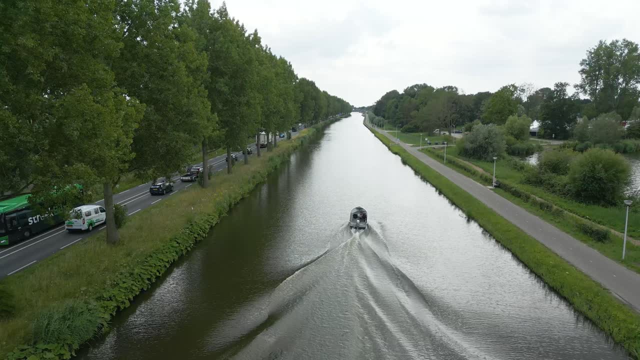 Drone footage of a motorboat on a canal near Alphen aan den Rijn, framed by trees and bike paths on both sides