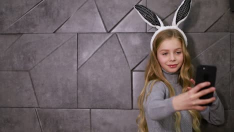 young girl in bunny ears taking a selfie with a smartphone