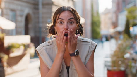 young woman looking surprised at camera shocked by sudden win good victory news wow in city street