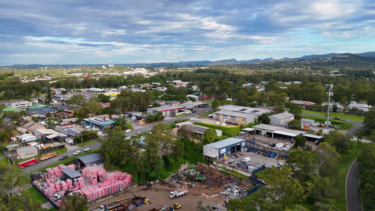 Aerial drone footage captures an industrial area in Gold Coast, Australia, showcasing warehouses, greenery, and vibrant skies