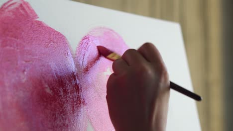 primer plano de un artista irreconocible pinta peonías rojas u otras flores con pincel en el lienzo. el artista pinta flores rosadas en el lienzo con pincel grueso, primer plano, vista lateral. luz solar natural sobre la imagen