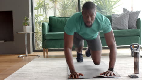exercising on yoga mat, african american man doing mountain climbers in living room, copy space