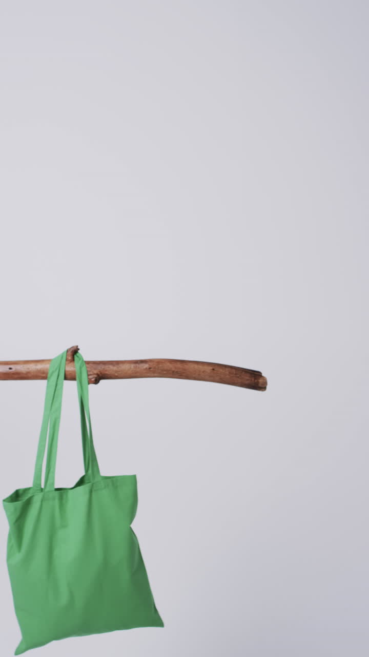 Vertical video of green canvas bag hanging from branch with copy space on white background