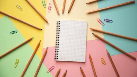 stop motion of a notebook, colorful paper clips and wooden pencils on pastel colored paper