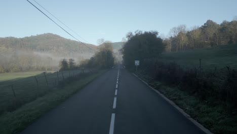 morning fog lingers over a narrow asphalt road winding through the green hills of a mediterranean landscape, creating a serene and picturesque scene at sunrise