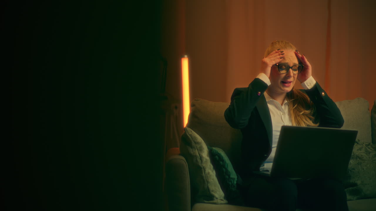 женщина нервничает, работая на ноутбуке поздно вечером.