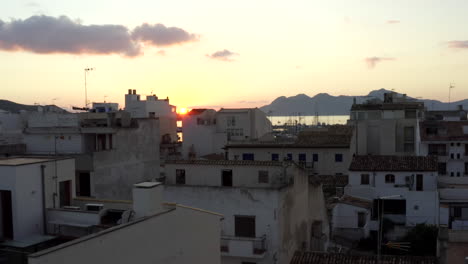 AERIAL:-Small-City-with-Port-on-Tropical-Island-with-Boats-and-Ocean-at-Small-Town-at-Sunrise-with-Mountains-in-Background-Vacation,-Travel,-Sunset