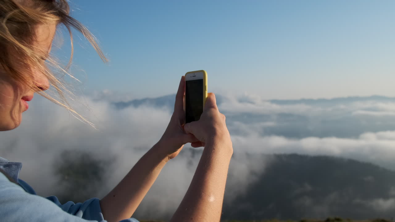 mujer tomando una foto de una vista de montaña con nubes