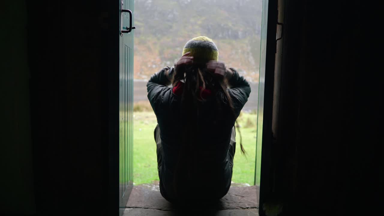 드레드록을 하고 하이킹 장비를 착용한 한 남자가 총에 맞아 스코틀랜드 고원의 좁은 출입구에 있는 계단에 앉아 야외 전망을 즐깁니다.