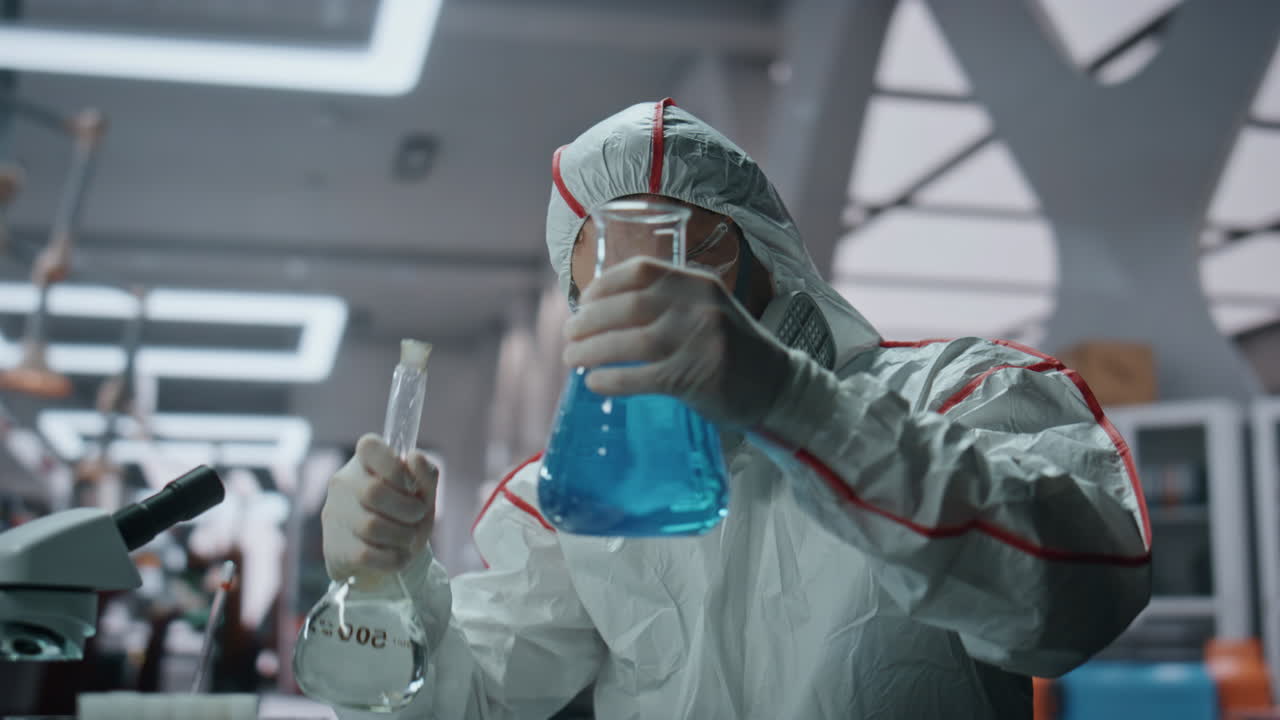 생화학자가 안전복을 입고 화학 액체로 실험실 병을 채우고 있습니다.
