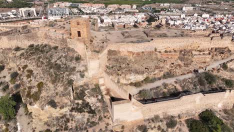 Flug-Mit-Einer-Drohne-Mit-Parallaxeffekt-über-Den-Höchsten-Teil-Der-Festung,-Wo-Menschen-Entlang-Der-Mauer-Laufen-Und-Im-Hintergrund-Die-Stadt-Sagunto-An-Einem-Wintermorgen-Zu-Sehen-Ist