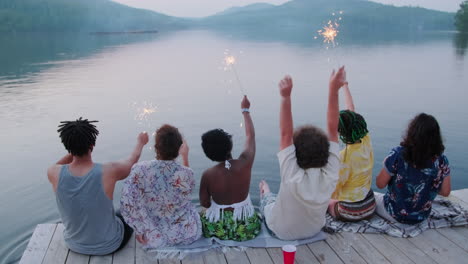 young people holding sparklers and waving arms on lake pier