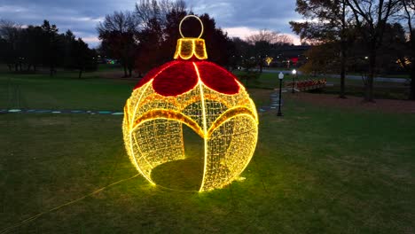 aerial orbiting shot of large lighting christmas ornament and bulb on grass field in american park during dusk in december