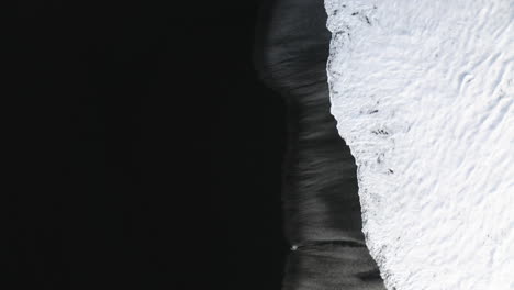 aerial split view of a black sand beach and foamy waves in cloudy stokksnes, iceland