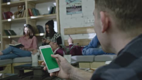 man using smart phone with green screen in office lounge area