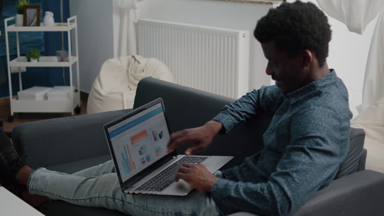 African american man working from home, remote working on laptop computer with online graphs and statistics