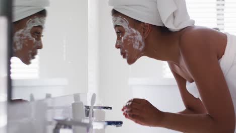 African-american-woman-washing-off-her-face-mask-in-the-bathroom-sink-at-home