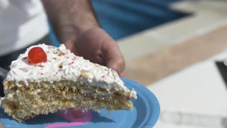 Sirviendo-Un-Trozo-De-Pastel-De-Celebración-En-Un-Plato-De-Papel-Azul-En-Una-Fiesta-De-Cumpleaños-Afuera-Cerca-De-Una-Piscina,-Detalle-En-Cámara-Lenta-Con-Enfoque-Suave