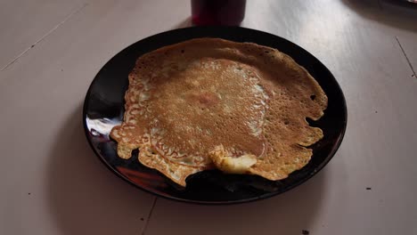 clumsy shaped pancake on a black plate on white table