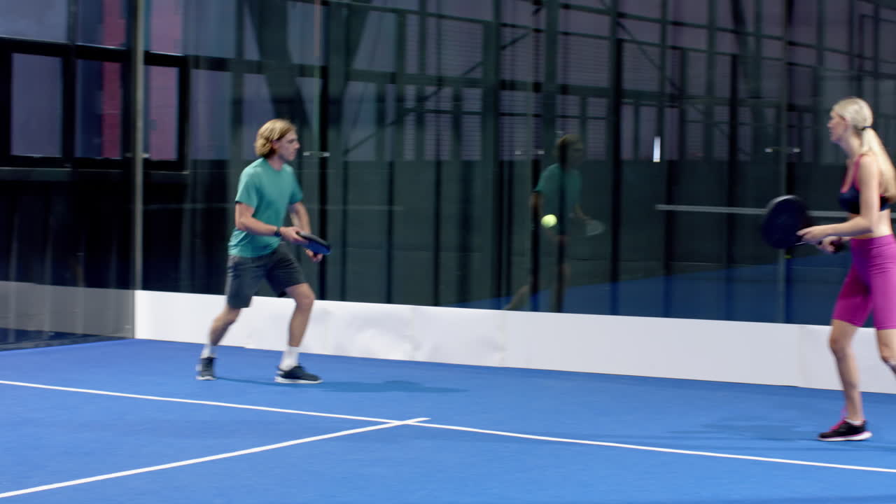 Playing padel tennis, man and woman focusing on hitting ball in indoor court