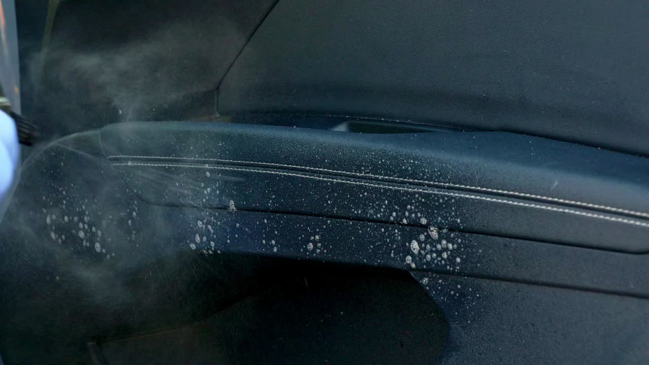 Spraying cleaning product on to white mark on black car interior leather door arm rest