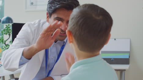 Médico-Sonriente-O-Médico-De-Cabecera-Con-Bata-Blanca-Reuniéndose-Con-Madre-E-Hijo-Para-Una-Cita-En-El-Consultorio