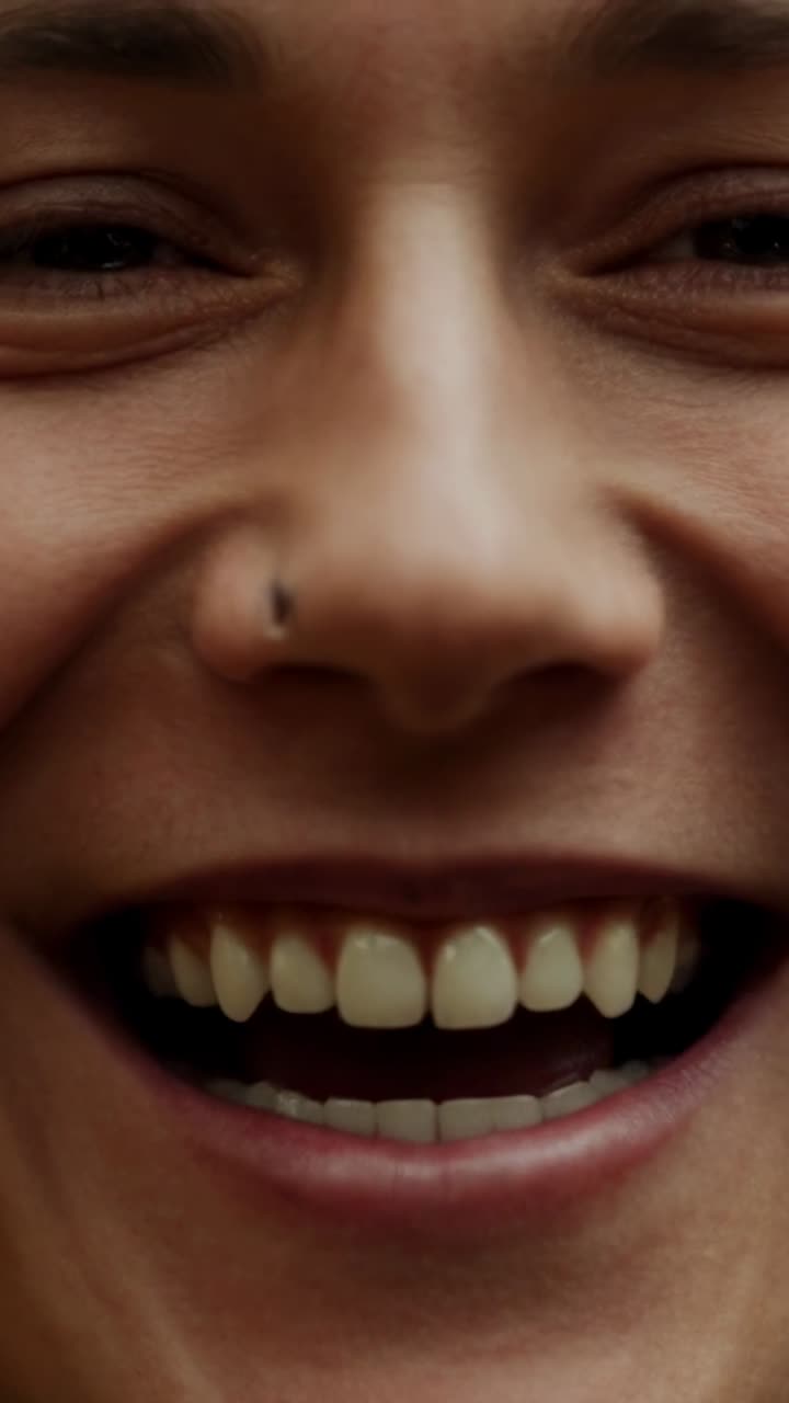 Vertical video: Smiling woman responding to camera in close-up, showing teeth and left nostril stud