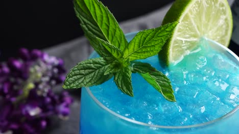 vibrant cocktail with a striking blue hue from blue curacao, mixed with the zesty of lime juice. vodka adds a smooth, bold finish, garnished with a lime wheel and fresh mint for a refreshing twist.