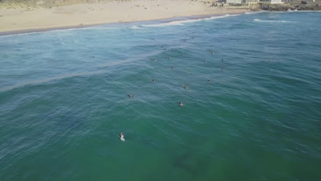 fotografía aérea de un dron volando sobre surfistas en las olas del océano atlántico, al atardecer, en praia do guincho, en una noche soleada, en la costa de cascais, en portugal