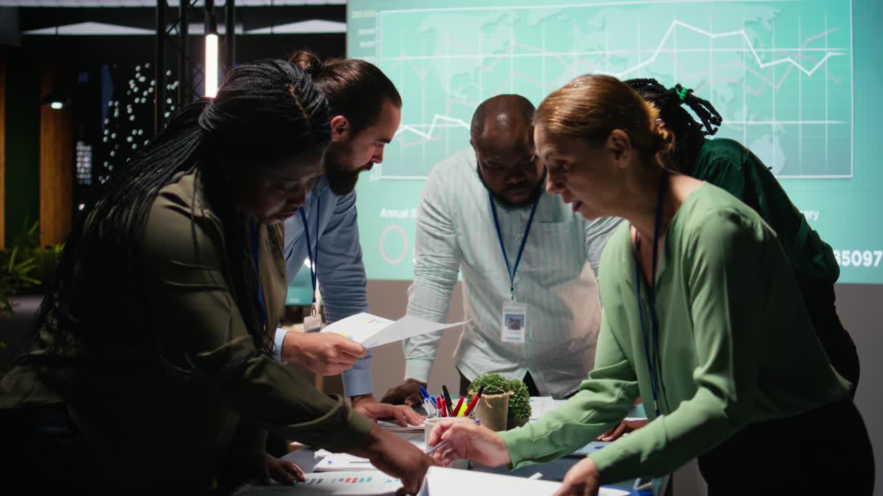 Multiethnic team exchanging files and review forecasting diagrams at night