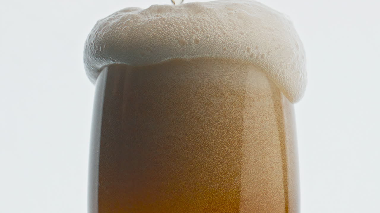 la espuma de vidrio de la cerveza se desborda de cerca. la mousse embriagadora se vierte sobre el borde del recipiente.