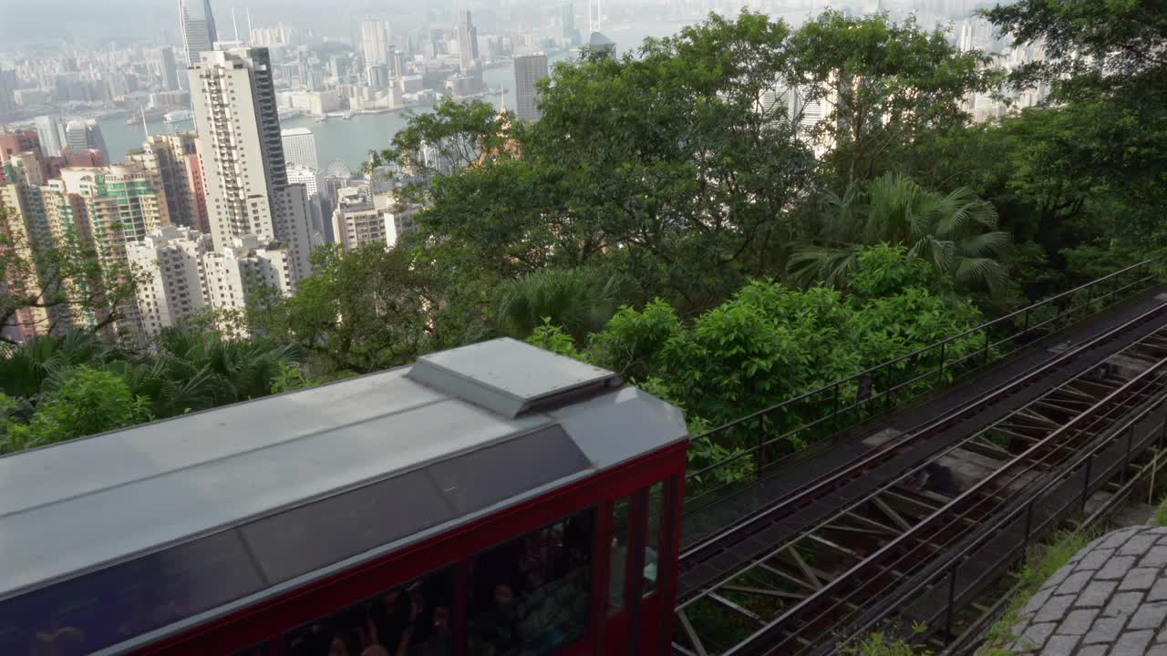 China,Hong Kong, Victoria Peak, Red Tram is coming down from Victoria Peak slowly inside the greenery on a sunny day. Beautiful Kowloon and skyscraper's view behind the tram and the greenery.