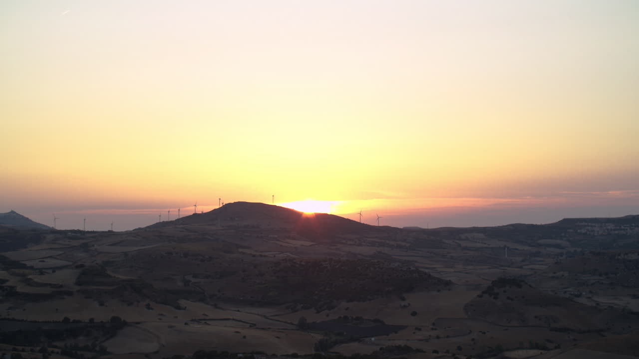 Sensational golden hour colorful sunset above field of renewable energy wind turbines onshore on top of hill in remote rural countryside land and landscape on sunny sky day, Sardinia, Italy, static