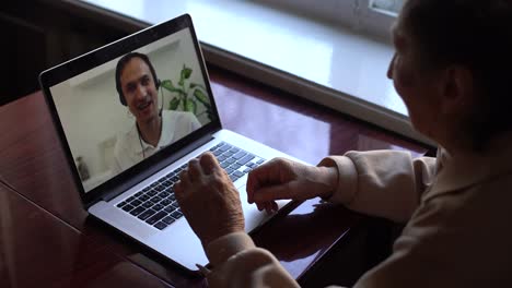 Communication-Concept.-Back-view-of-granny-making-video-call-on-laptop,-chatting-with-grandchildren