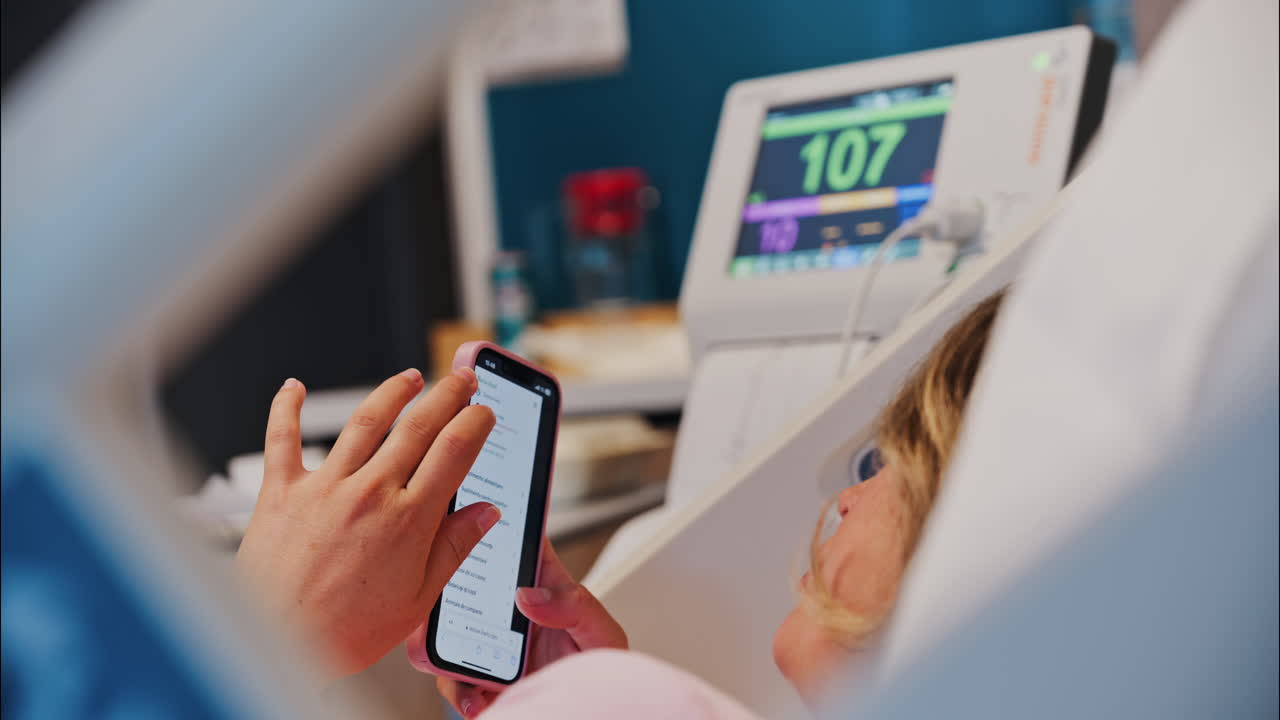 Chisinau, Moldova - May 31, 2025: Pregnant woman using the iHerb app on her phone while doing a prenatal check-up at the doctor's office