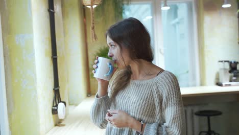 young european female student is enjoying her coffee or tea at the coffeehouse with natural background