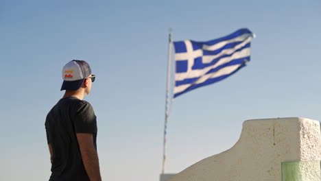 one man stands next to a waving greek flag