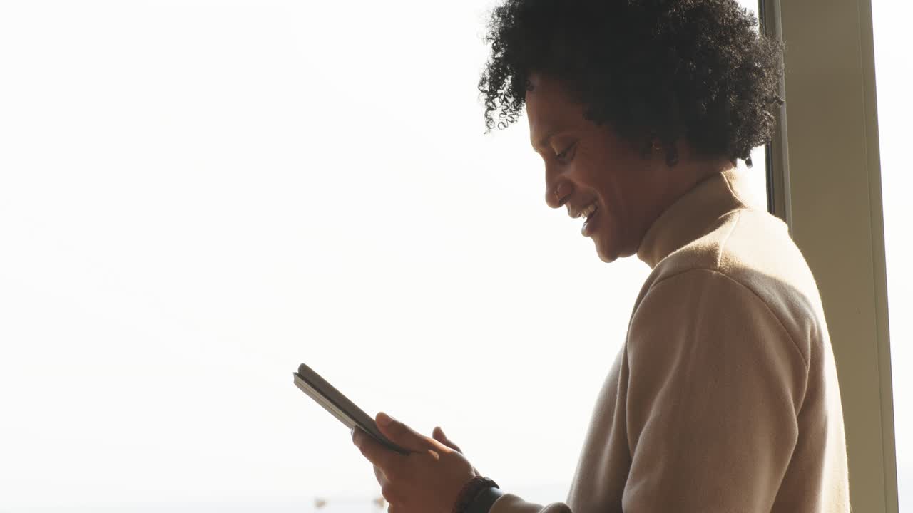 African American man entering lit room tapping tablet with wristband browsing messages, copy space