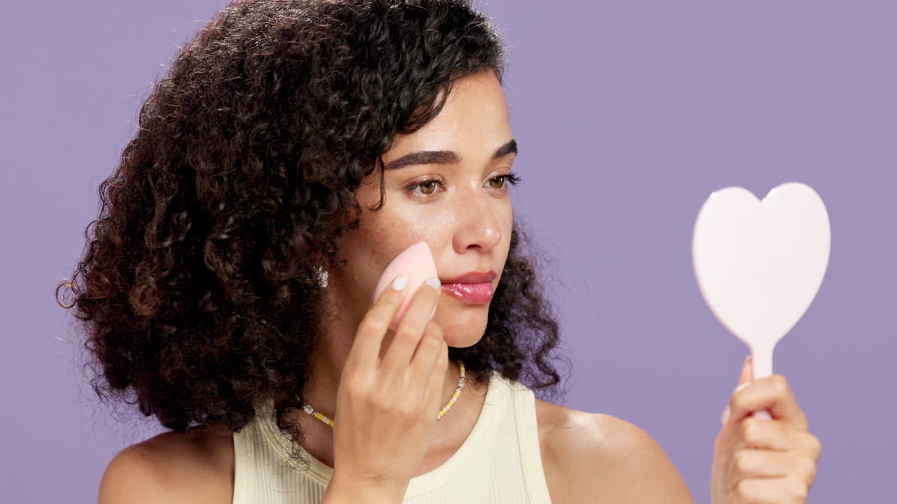 Woman applying makeup with a sponge and looking in a heart-shaped mirror