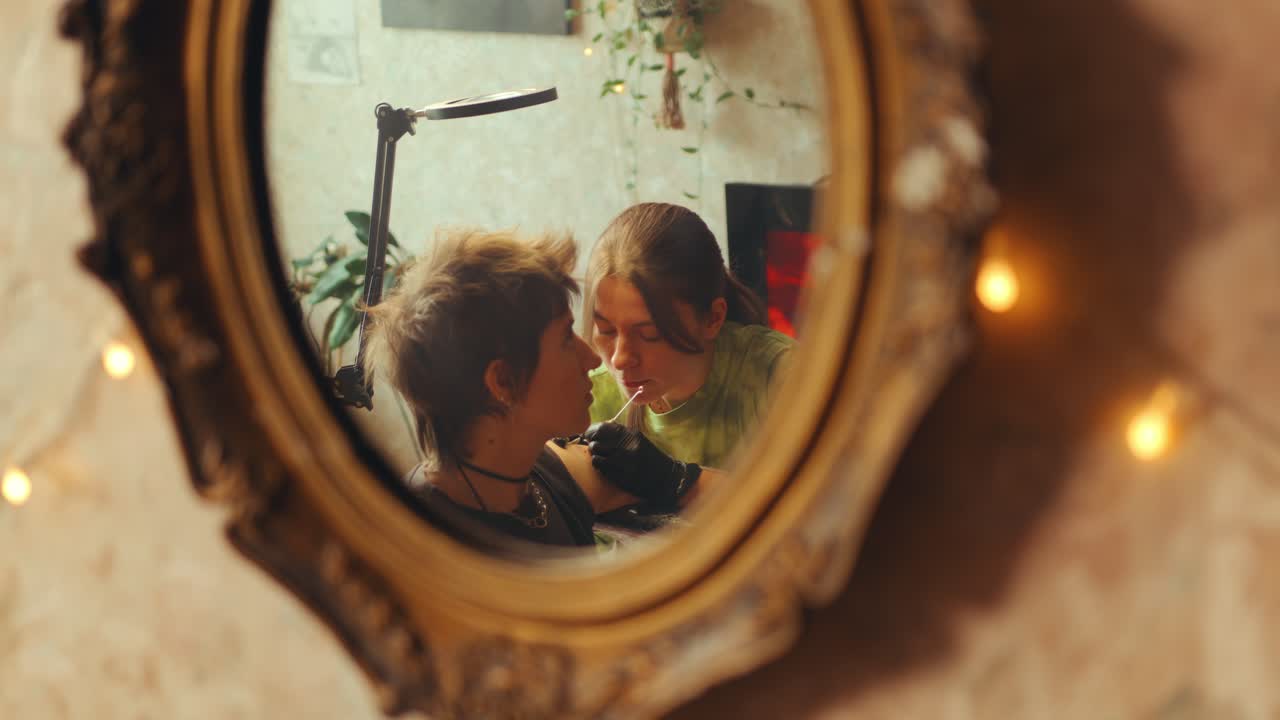 Mirror Reflection of Female Tattoo Artist Doing Upper Arm Tattoo for Woman