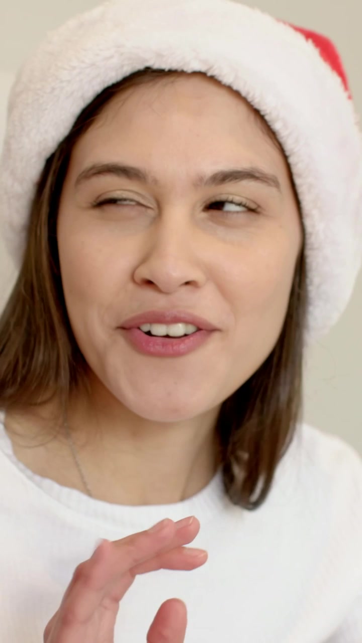 Vertical video: Starting closed-eyed, woman wearing Santa hat expressing holiday cheer at home