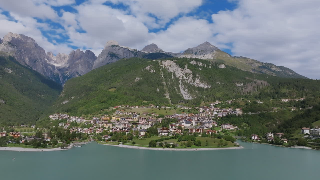 Wide aerial video moving away from the town of Molveno with the lake in the foreground in northern Italy with the Dolomite mountains in the background.